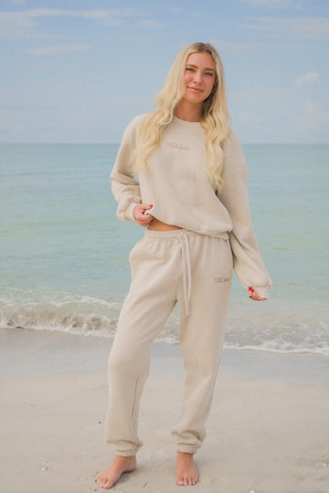 Woman wearing the SRQutie Logo Sweatpants in beige with the matching sweatshirt, on the beach