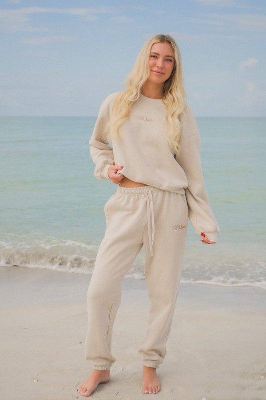 Woman wearing the SRQutie Logo Sweatpants in beige with the matching sweatshirt, on the beach