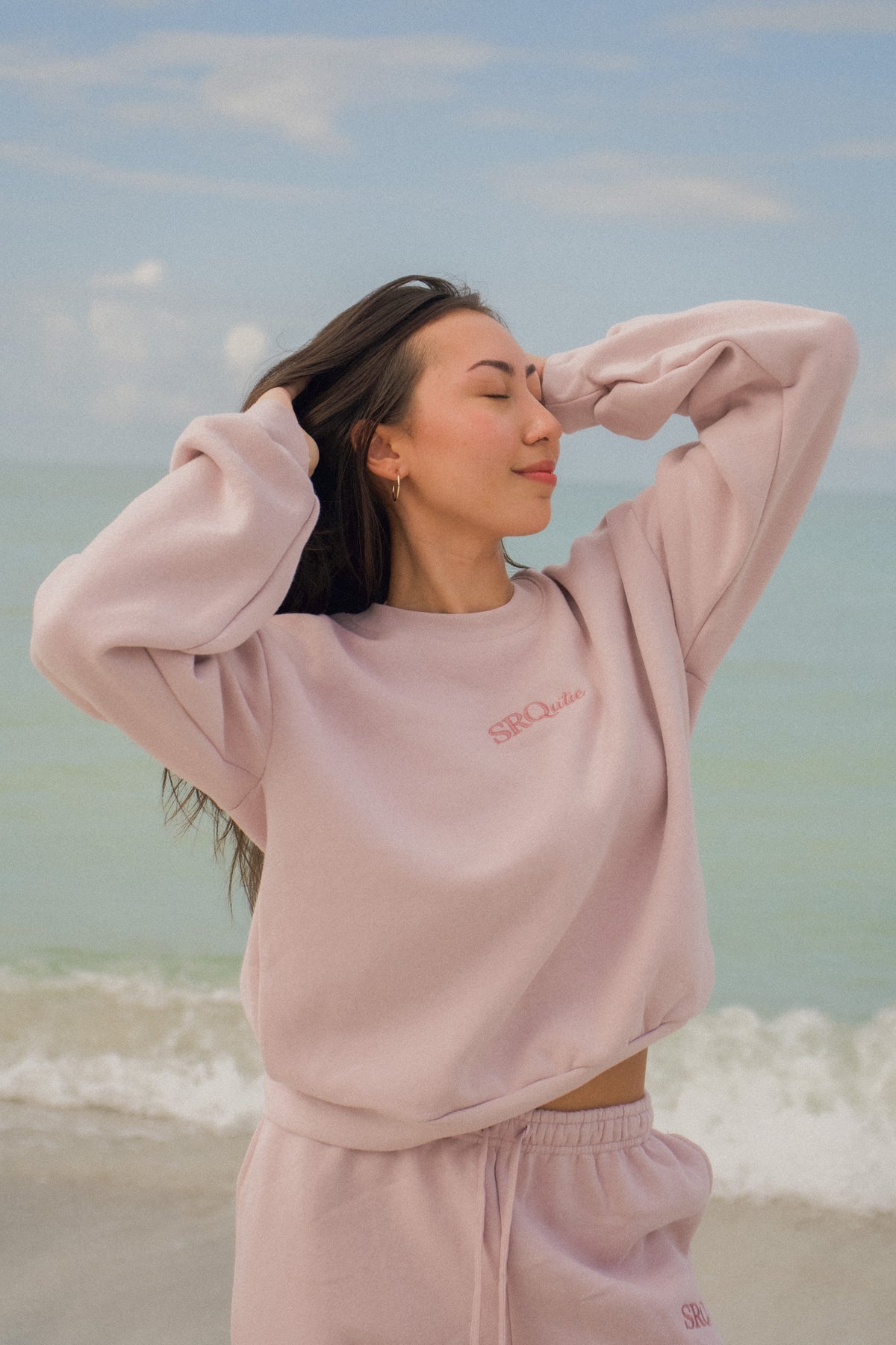 Woman on the beach wearing the SRQutie Logo Sweatshirt in Blush with the matching Logo Sweatpants