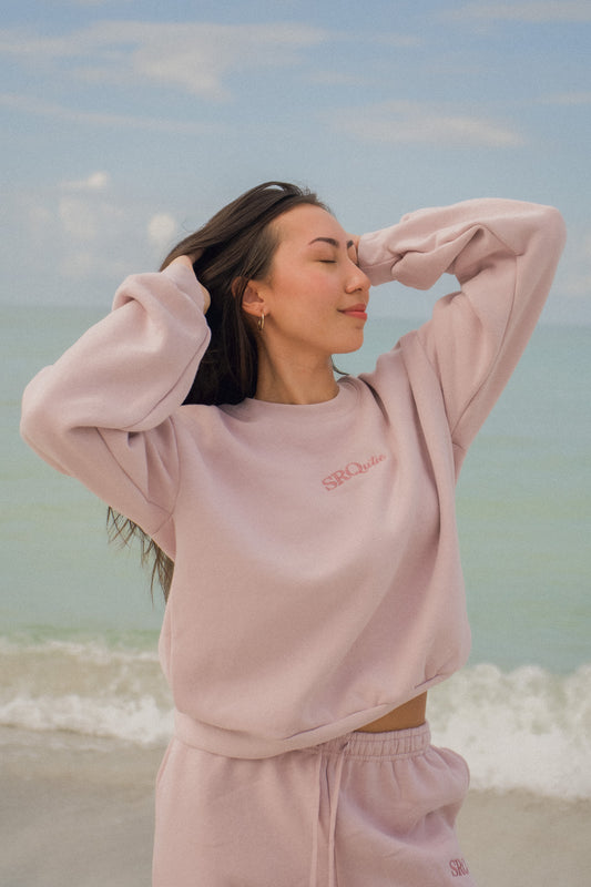 Woman on the beach wearing the SRQutie Logo Sweatshirt in Blush with the matching Logo Sweatpants