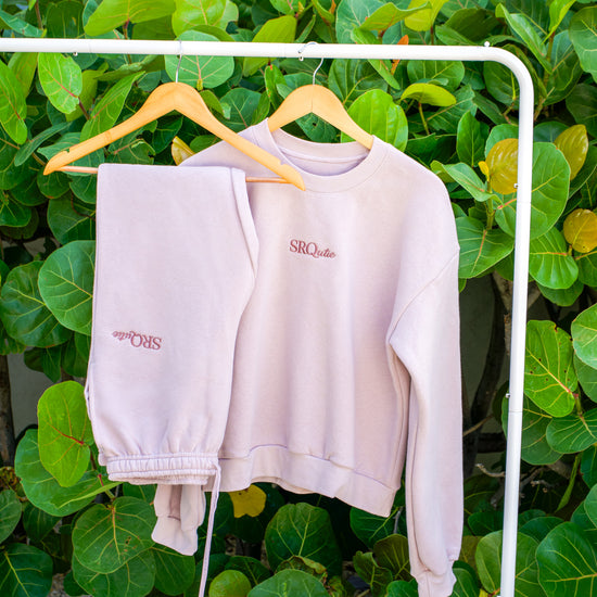The SRQutie Logo Sweatshirt and matching Logo Sweatpants in Blush, on a hanging rack