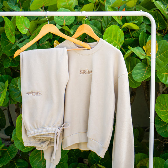 The SRQutie Logo Sweatshirt and matching Logo Sweatpants in Cream, on a hanging rack