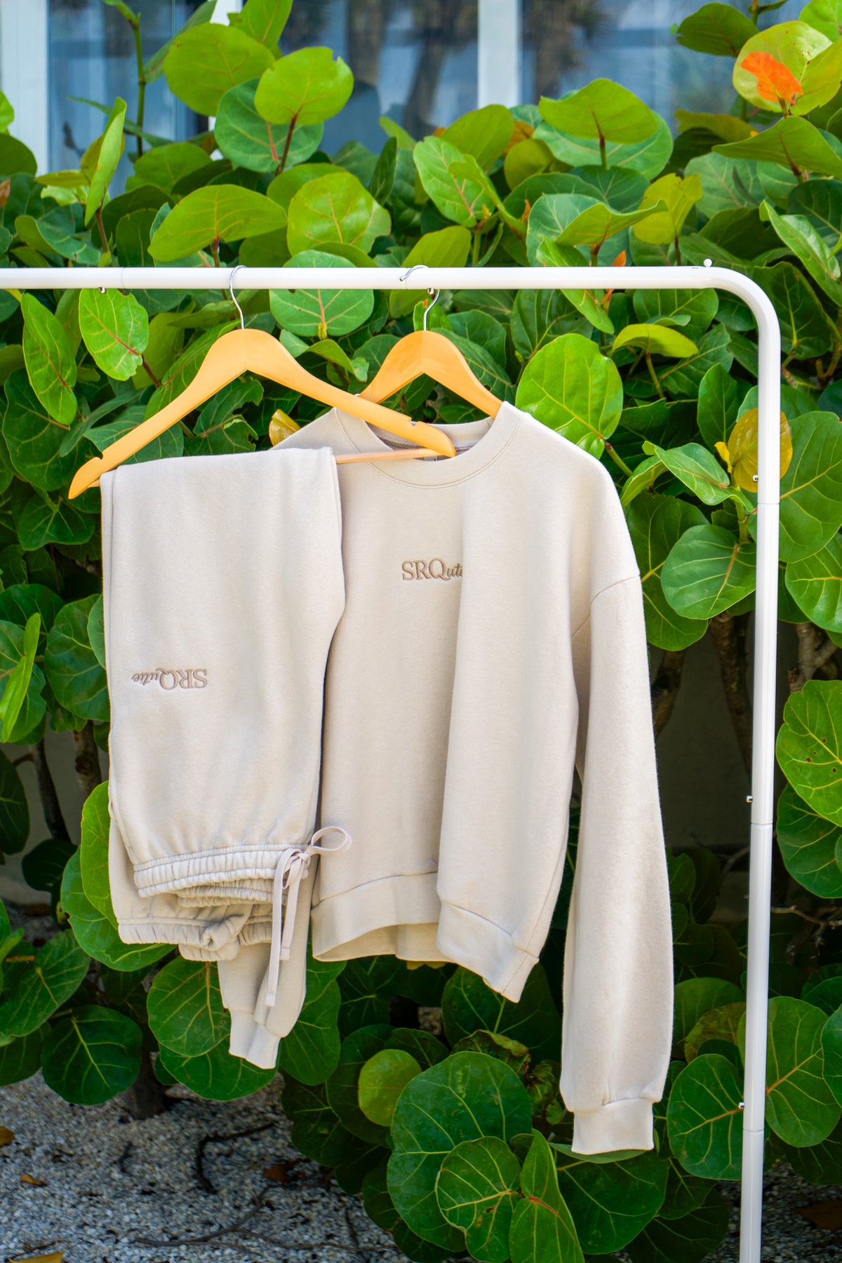 The SRQutie Logo Sweatshirt and matching Logo Sweatpants in Cream, on a hanging rack